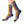 A pair of crew socks worn on a person's legs, featuring a colorful vertical stripe pattern in purple, yellow, and teal with a repeating pattern of cartoon cat faces, finished with black heels and toes.