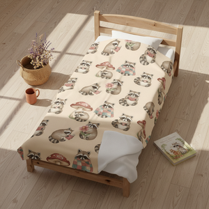 A wooden single bed in a sunlit room, covered with a cream-colored blanket printed all over with raccoons and mushroom motifs. A woven basket with dried flowers, a small orange mug, and a children's book sit nearby on the light wood floor.