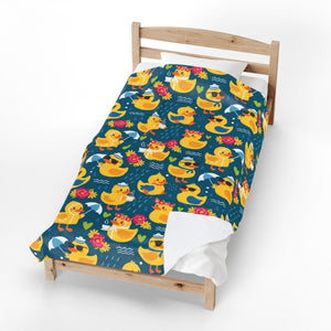 A toddler single bed with a light natural wood frame, styled with a dark teal blue comforter featuring a colorful cartoon rubber duck pattern, white sheets, and a white pillow against a clean white background.