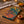 A square decorative textile or wall hanging featuring a festive Diwali-inspired mandala design with orange marigold garlands, lit oil lamps, and a teal background.