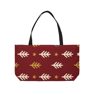 A rectangular tote bag with a dark red background, featuring a repeating pattern of cream-colored stylized pine trees and small gold stars, with black shoulder straps, shown against a plain white background.