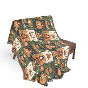 A fringed woven throw blanket draped over a brown armchair, featuring a patchwork pattern of illustrated woodland animals in earthy green, brown, beige, and cream tones on a white studio background.