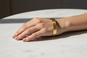 A gold metal cuff bracelet engraved with the words 'find your purpose' in black lettering, worn on a person's wrist resting on a white marble surface.