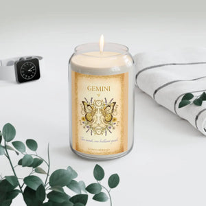 Candle with a Gemini-themed label on a white surface with a plant and watch in the background